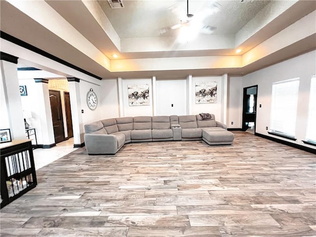 living room with light hardwood / wood-style floors, a tray ceiling, and decorative columns