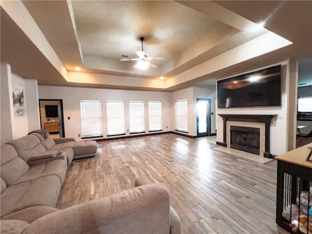 living room with light hardwood / wood-style floors, a tray ceiling, and ceiling fan