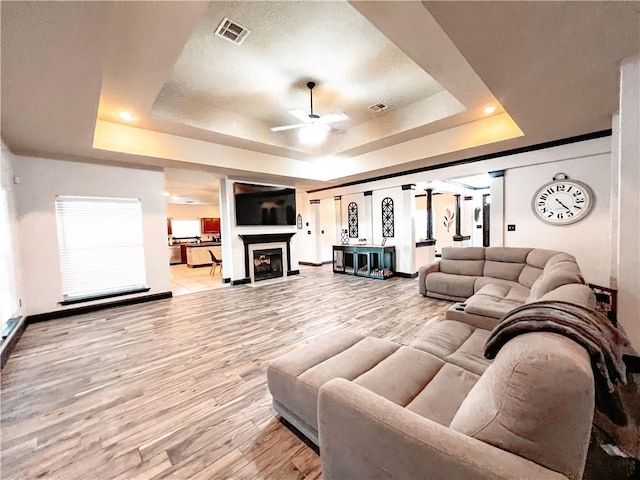 living room with light hardwood / wood-style flooring, a tray ceiling, and ceiling fan