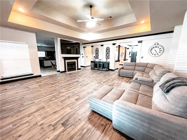 living room featuring ceiling fan, wood-type flooring, and a tray ceiling