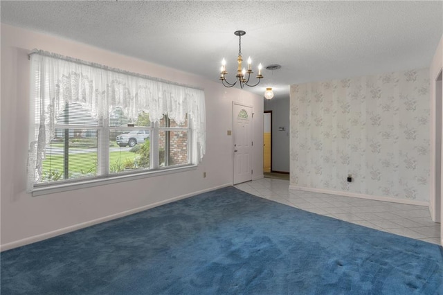 spare room featuring a textured ceiling, carpet, and an inviting chandelier