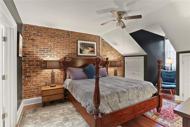 bedroom featuring light wood-type flooring, vaulted ceiling, ceiling fan, and brick wall