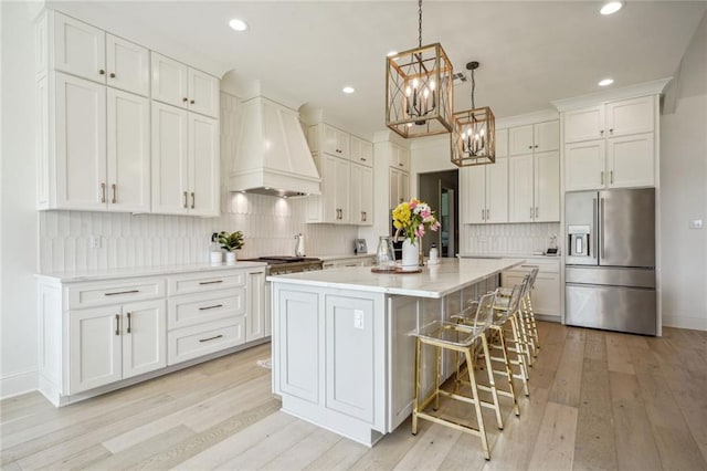 kitchen with a kitchen island, light wood-type flooring, stainless steel refrigerator with ice dispenser, and premium range hood