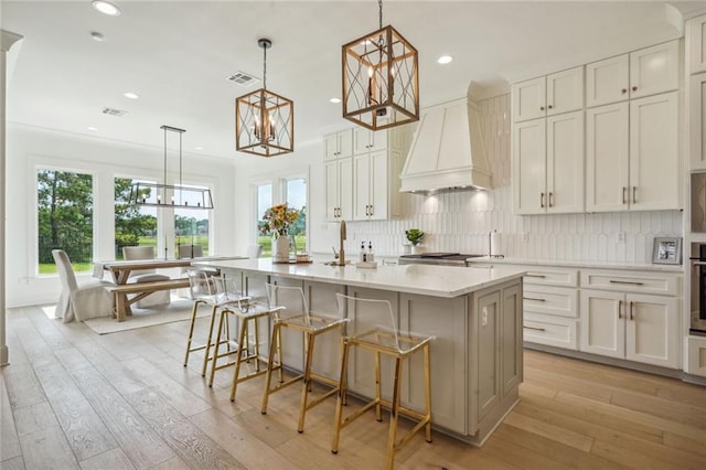 kitchen with white cabinetry, light wood-type flooring, an island with sink, a breakfast bar area, and custom exhaust hood