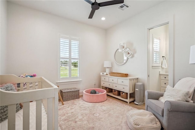 bedroom featuring a nursery area, hardwood / wood-style floors, ceiling fan, and ensuite bathroom