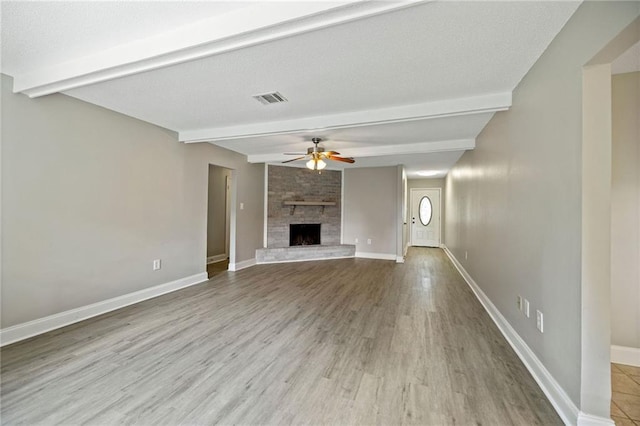 unfurnished living room with ceiling fan, a large fireplace, visible vents, baseboards, and beamed ceiling