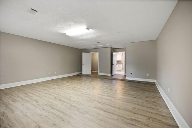 empty room with baseboards, a textured ceiling, visible vents, and wood finished floors