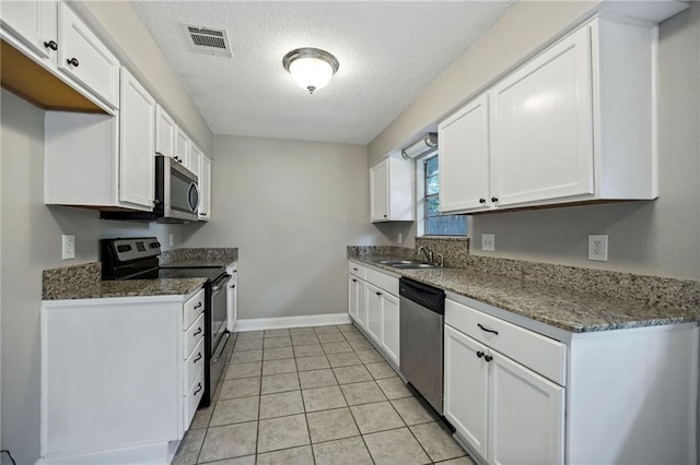 kitchen with stainless steel appliances, dark stone countertops, sink, and white cabinetry