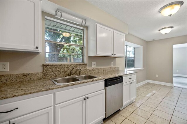 kitchen with light tile patterned floors, light stone counters, white cabinetry, sink, and stainless steel dishwasher