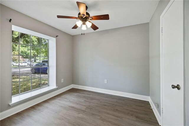 empty room with dark wood-type flooring, plenty of natural light, and ceiling fan