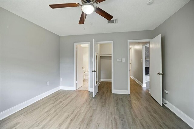 unfurnished bedroom with a closet, ceiling fan, a spacious closet, and light wood-type flooring