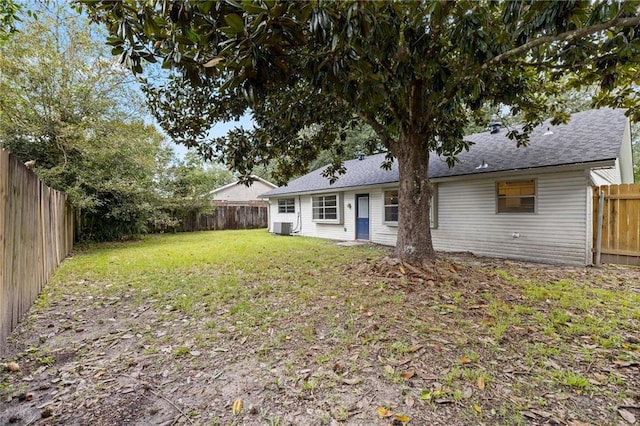 back of house featuring a yard, roof with shingles, a fenced backyard, and central air condition unit