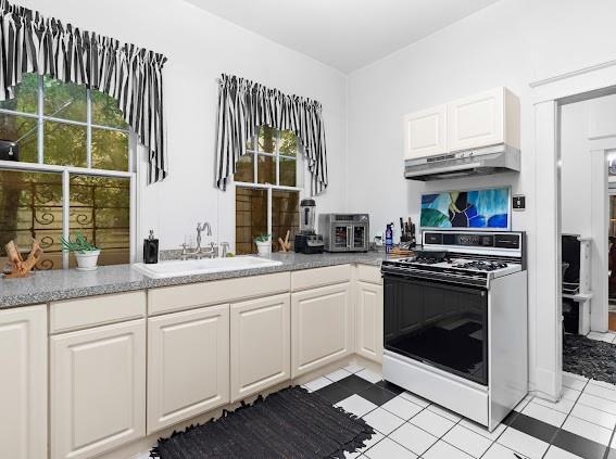 kitchen featuring white stove, a wealth of natural light, light tile patterned floors, and sink