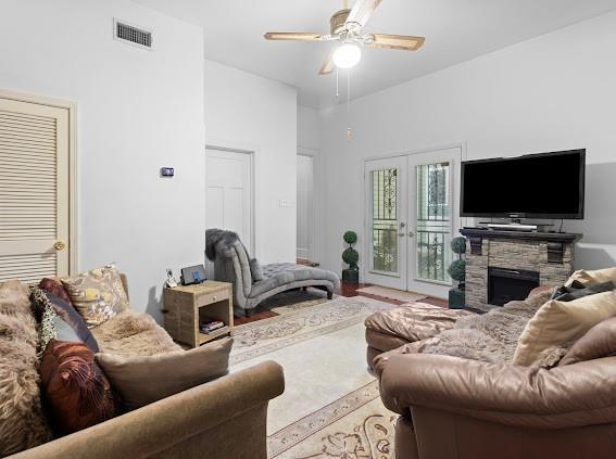 living room featuring ceiling fan, a fireplace, and french doors