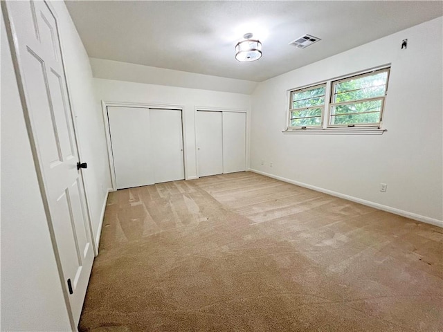 unfurnished bedroom featuring light carpet, vaulted ceiling, and multiple closets