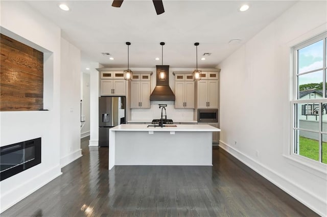 kitchen featuring an island with sink, ceiling fan, dark wood-type flooring, appliances with stainless steel finishes, and custom range hood