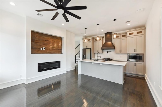 kitchen with decorative light fixtures, premium range hood, an island with sink, stainless steel appliances, and ceiling fan