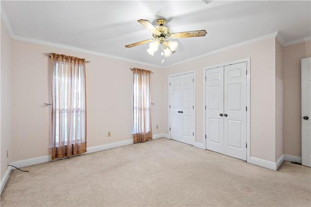 unfurnished bedroom featuring crown molding, light colored carpet, ceiling fan, and multiple closets