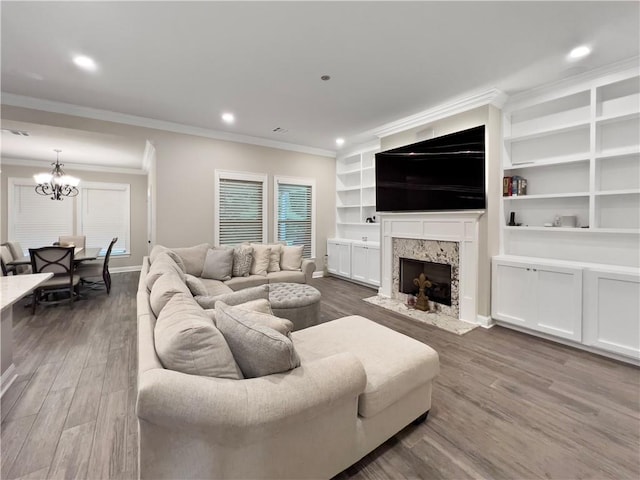 living room featuring hardwood / wood-style flooring, a fireplace, an inviting chandelier, ornamental molding, and built in features