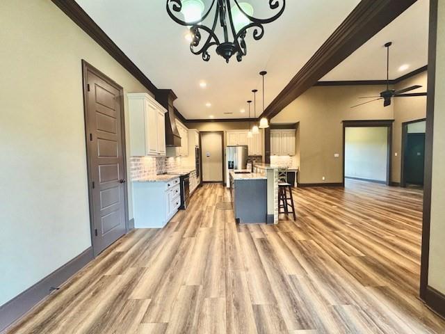 kitchen featuring decorative light fixtures, white cabinetry, a breakfast bar area, a center island with sink, and ornamental molding