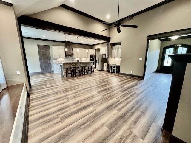 unfurnished living room featuring light wood-type flooring, beamed ceiling, a high ceiling, ceiling fan, and ornamental molding