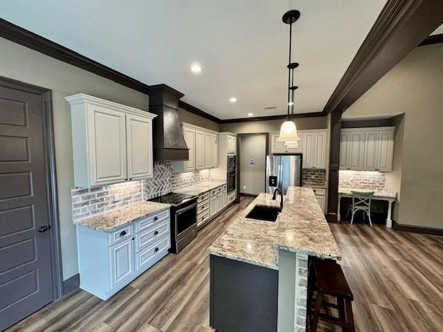 kitchen featuring custom range hood, stainless steel appliances, white cabinetry, sink, and an island with sink