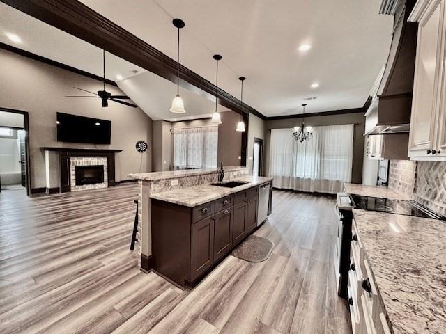 kitchen featuring light hardwood / wood-style flooring, decorative light fixtures, a brick fireplace, ceiling fan with notable chandelier, and light stone countertops