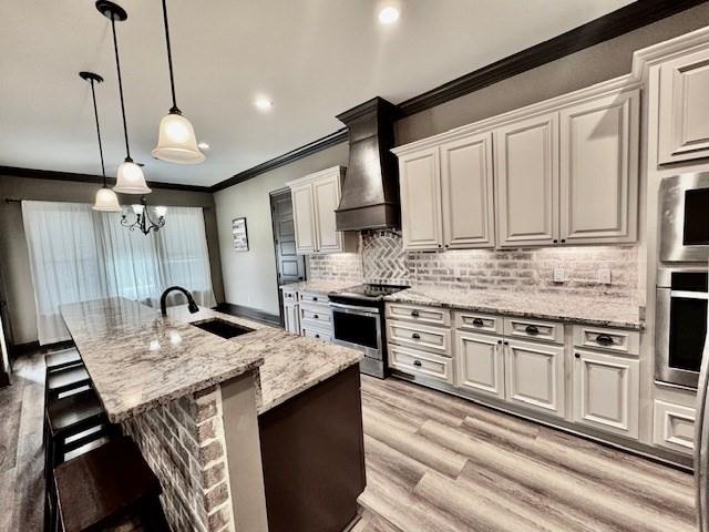 kitchen featuring decorative light fixtures, light hardwood / wood-style flooring, an island with sink, stainless steel appliances, and sink