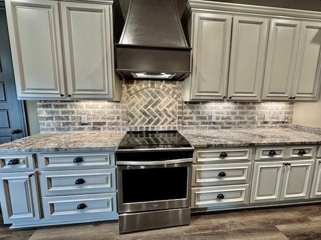 kitchen featuring tasteful backsplash, dark hardwood / wood-style flooring, stainless steel electric stove, light stone counters, and premium range hood