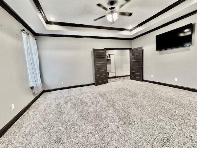 unfurnished bedroom with light colored carpet, ceiling fan, a raised ceiling, and ornamental molding