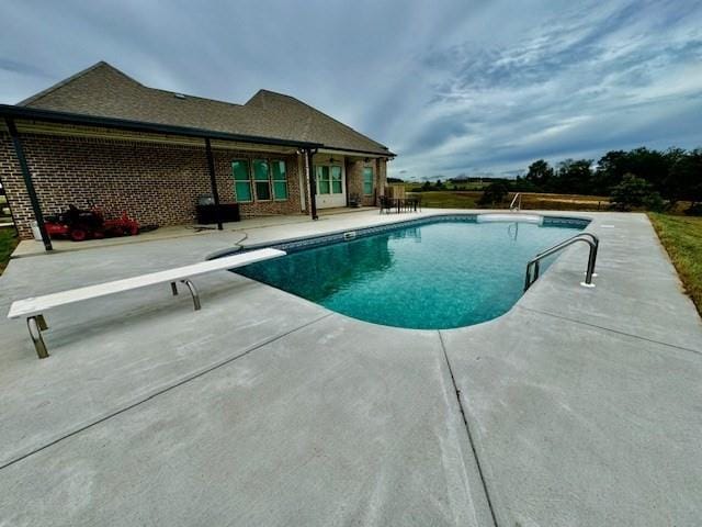 view of pool with a diving board and a patio