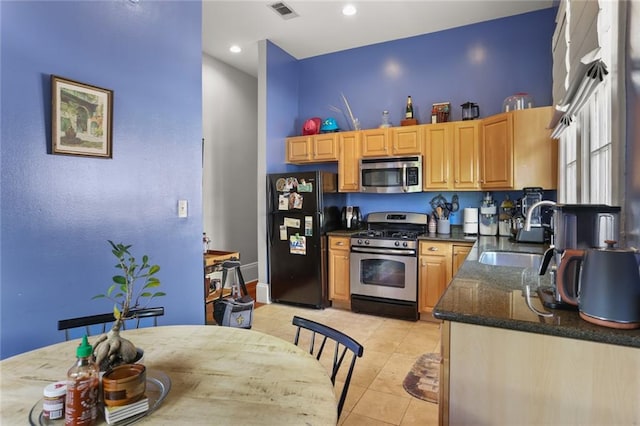 kitchen featuring appliances with stainless steel finishes, light tile patterned floors, dark stone counters, and sink