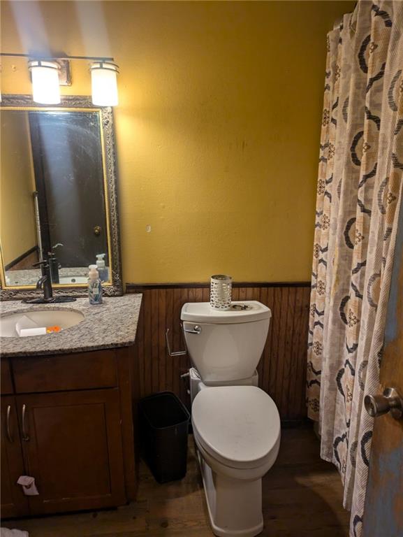 bathroom featuring wood-type flooring, wood walls, vanity, and toilet