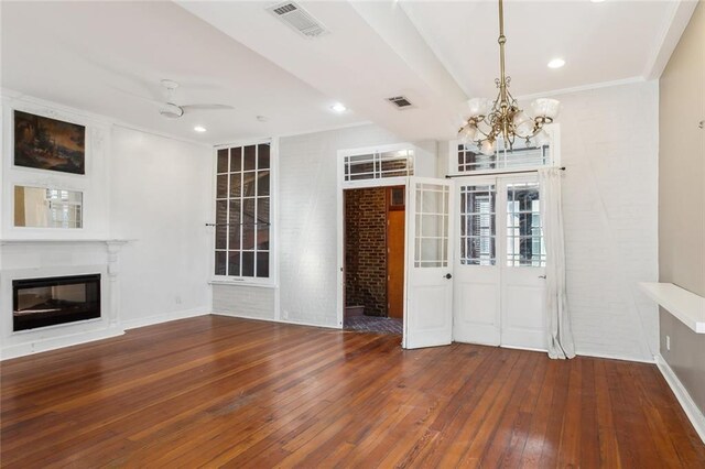 unfurnished living room with crown molding, brick wall, ceiling fan with notable chandelier, and hardwood / wood-style floors