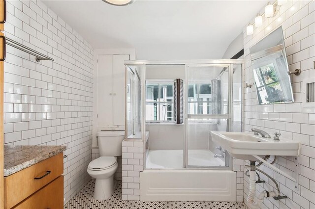 bathroom with bath / shower combo with glass door, tile walls, tile patterned floors, and toilet