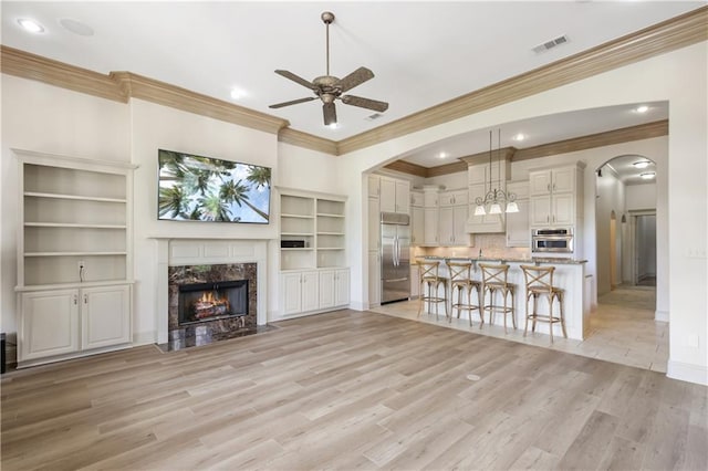 unfurnished living room featuring ceiling fan, ornamental molding, a premium fireplace, and light hardwood / wood-style flooring