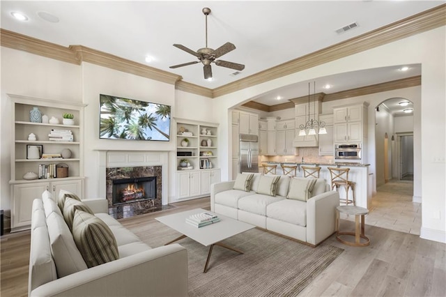 living room featuring ceiling fan, ornamental molding, a fireplace, and light wood-type flooring