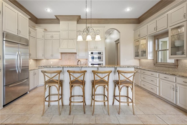 kitchen with a breakfast bar area, light stone counters, pendant lighting, stainless steel appliances, and a kitchen island with sink