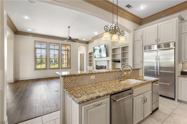 kitchen featuring sink, appliances with stainless steel finishes, a kitchen island with sink, white cabinets, and decorative light fixtures