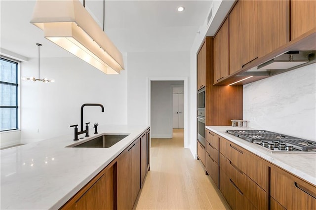 kitchen featuring light hardwood / wood-style flooring, decorative light fixtures, light stone counters, stainless steel appliances, and sink