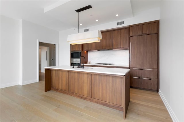 kitchen featuring light wood-type flooring, pendant lighting, gas stovetop, oven, and an island with sink