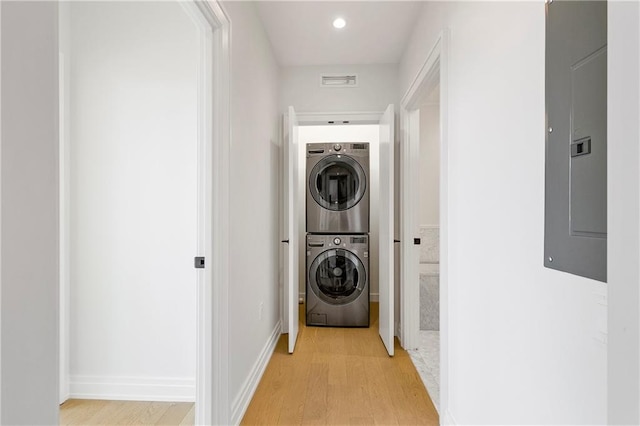 washroom featuring electric panel, stacked washer / drying machine, and light hardwood / wood-style floors