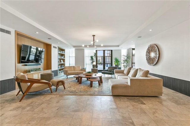 living room featuring built in features, a raised ceiling, and a notable chandelier