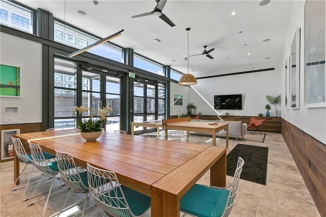 dining room featuring a wall of windows, ceiling fan, and wood walls