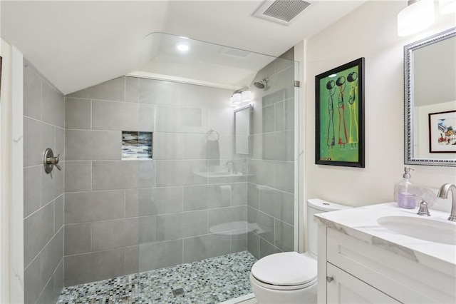 bathroom with vanity, lofted ceiling, a tile shower, and toilet