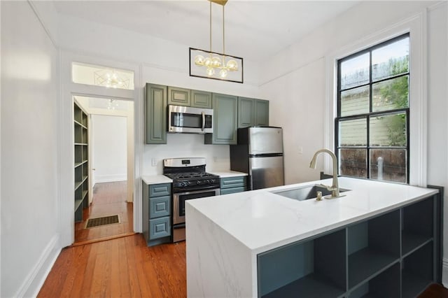 kitchen with light hardwood / wood-style floors, sink, stainless steel appliances, and hanging light fixtures