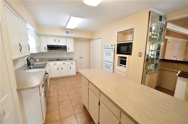 kitchen with black microwave, sink, double oven, light tile patterned floors, and white cabinetry