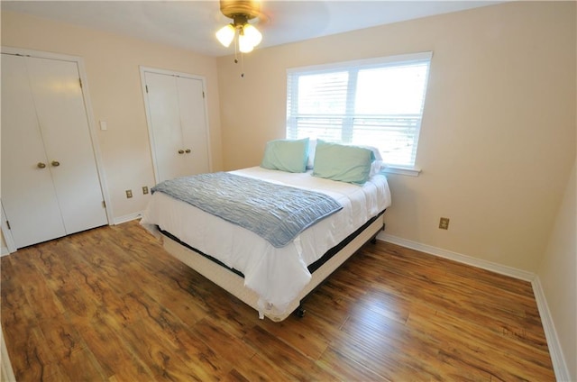 bedroom featuring dark hardwood / wood-style floors, multiple closets, and ceiling fan