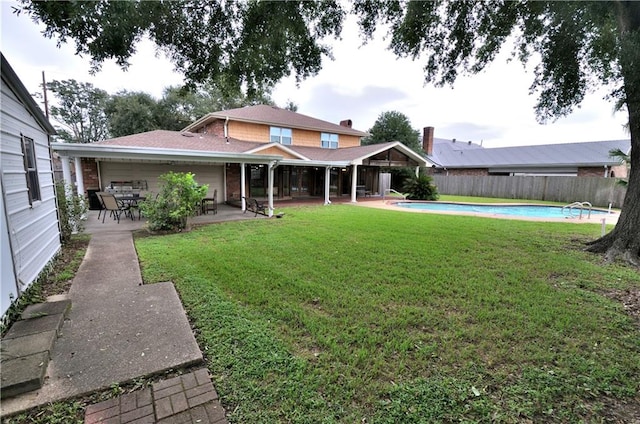 rear view of property featuring a yard, a fenced in pool, and a patio