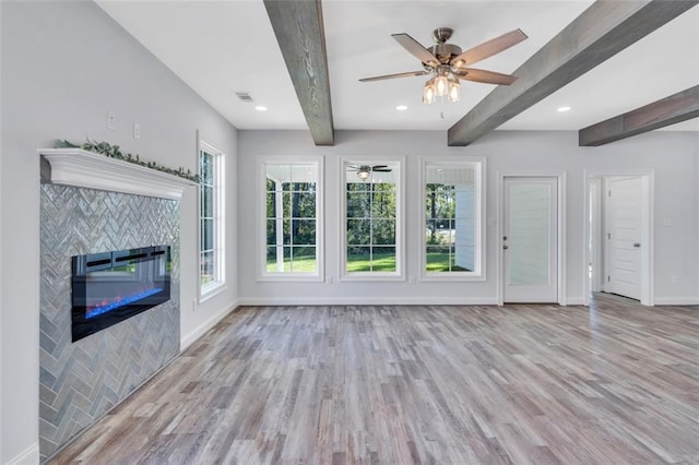 unfurnished living room featuring light wood-type flooring, a tile fireplace, ceiling fan, and a wealth of natural light